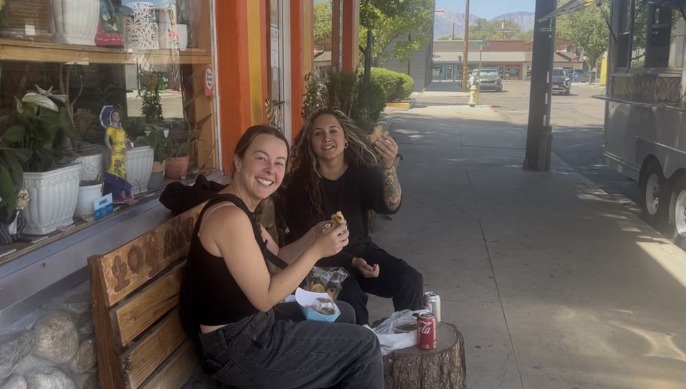 Two friends eating tacos on the bench outside