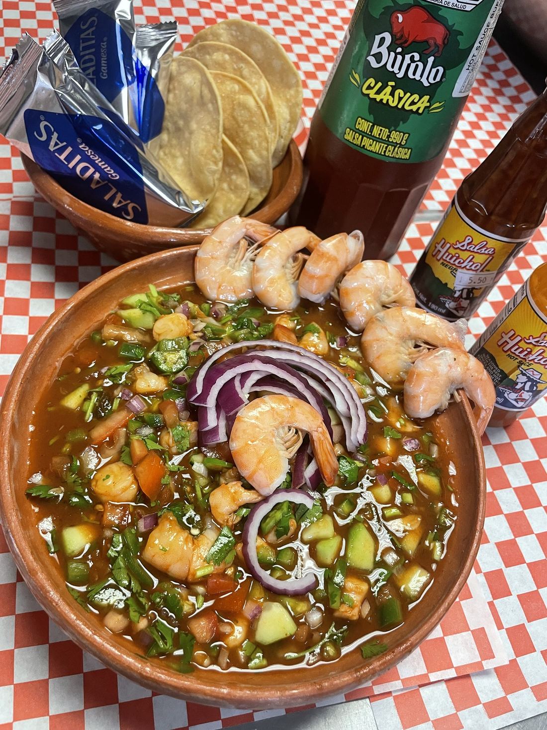 Shrimp cocktail in a clay bowl with tostadas and hot sauces