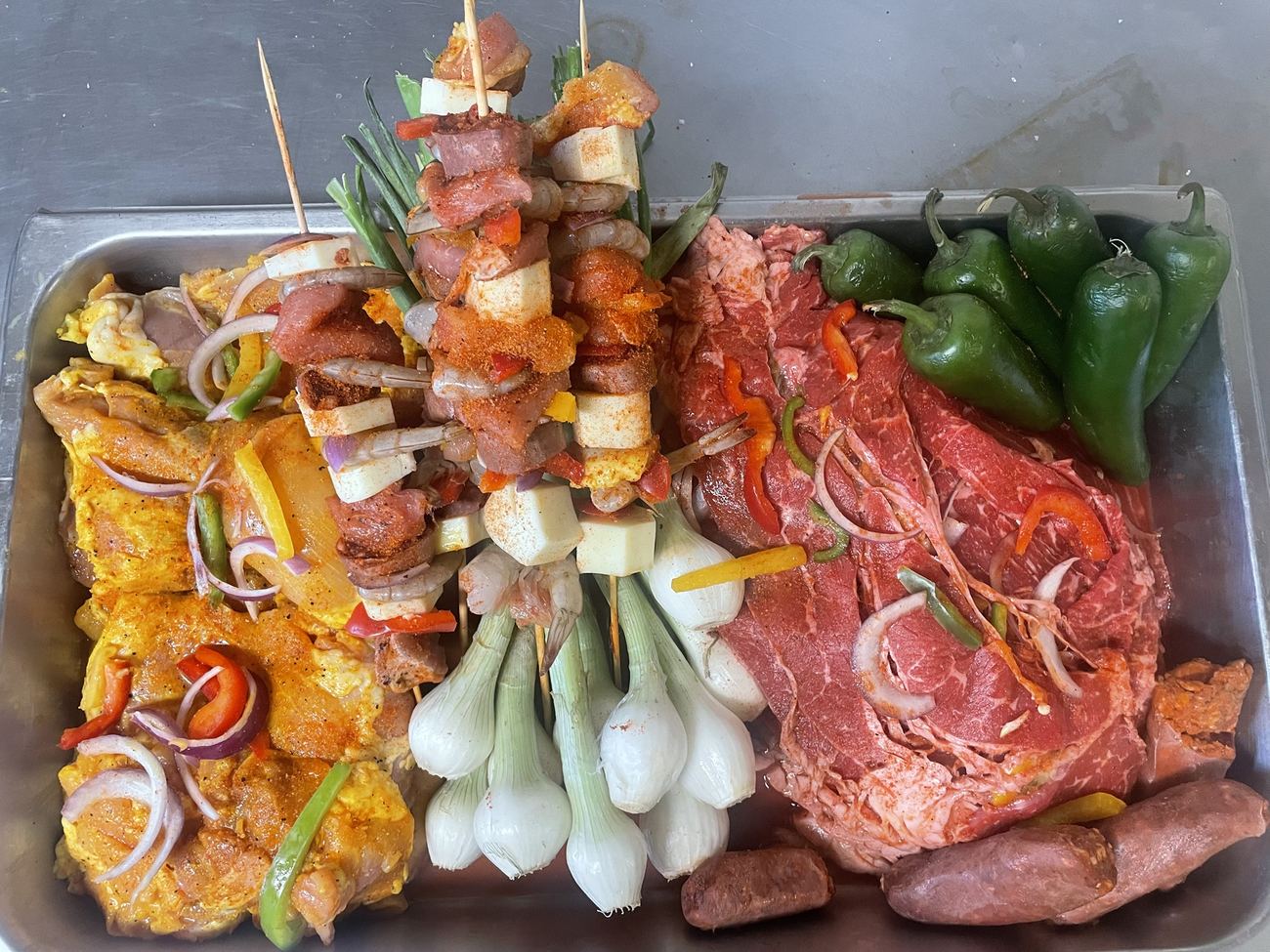 Tray of marinated chicken, beef, chorizo, shrimp and cheese skewers with green onions and jalapeños