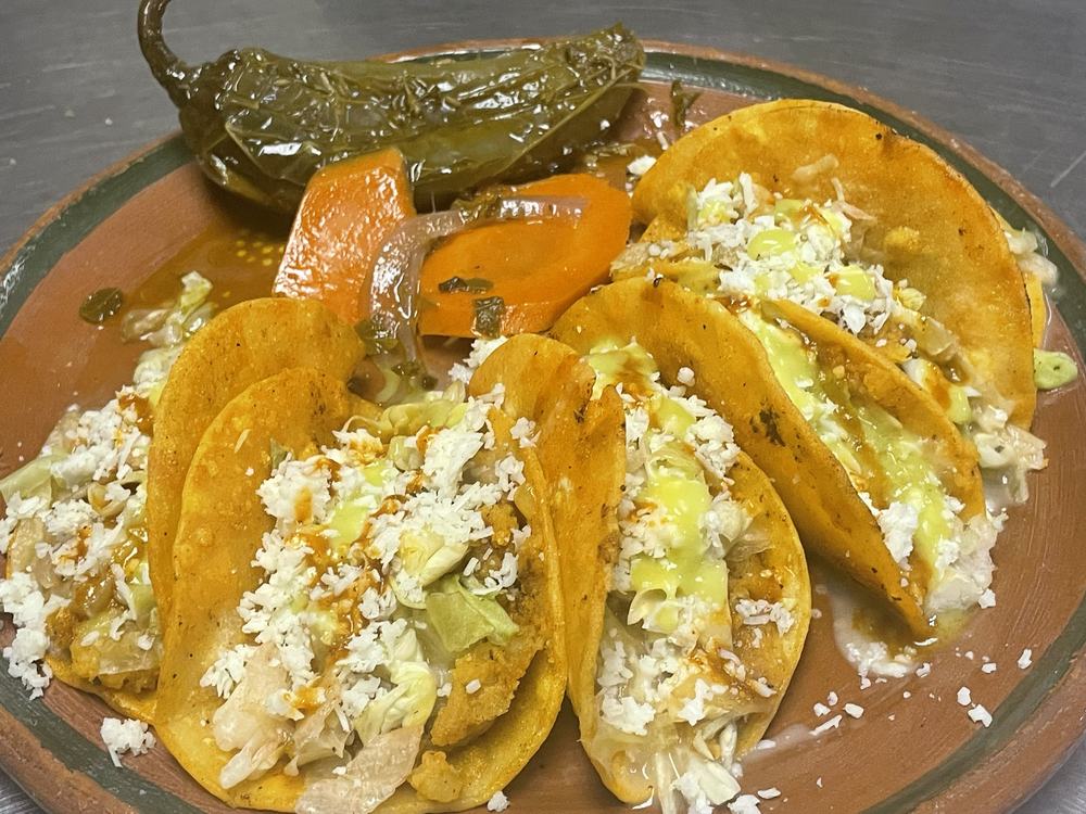 Crispy tacos with cabbage, cheese and crema, pickled carrots and a jalapeño