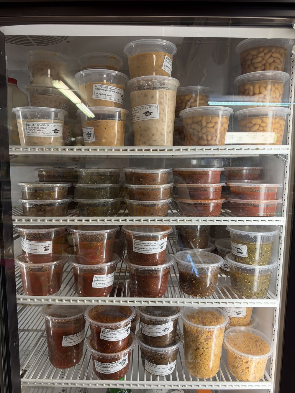 Fridge stocked with house-made refried beans and salsas in Las Adelitas Market containers